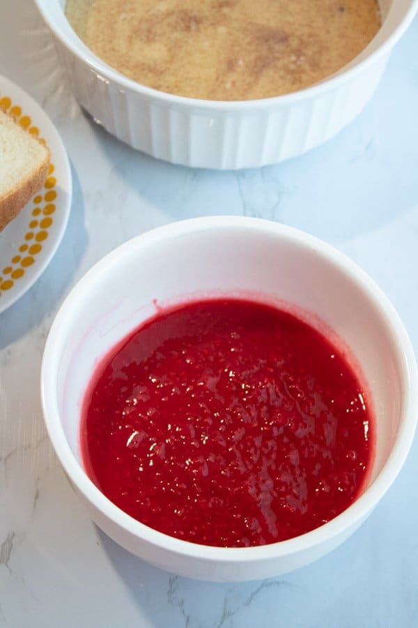 Raspberry syrup in a bowl ready to mix with the egg mixture in a separate bowl and bread on a plate on the side.