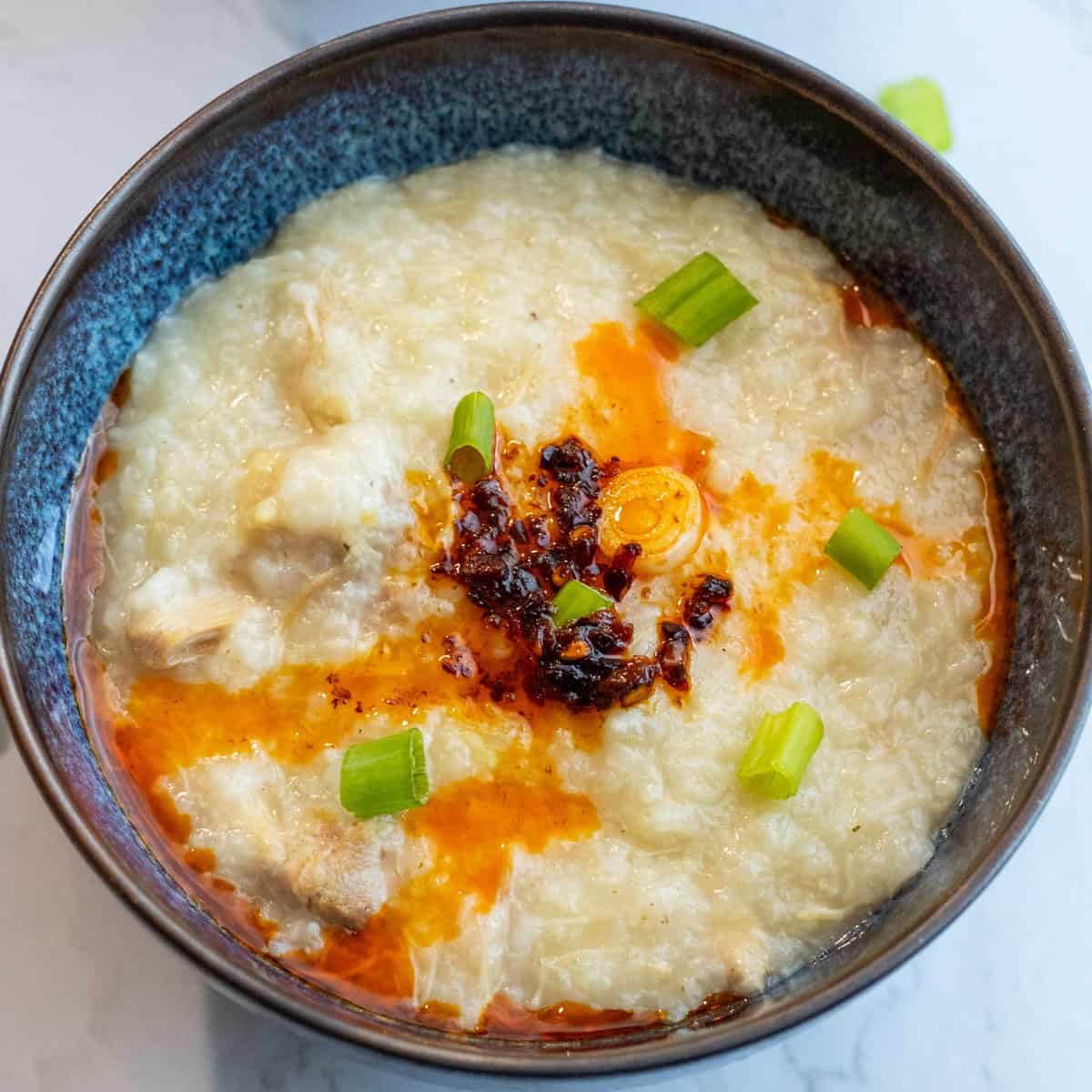 chicken congee served in a bowl with green onions and chili oil on top.