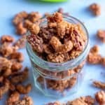 Candied Cashews and Pecans in a mason jar on a white background with nuts spilled on the sides of the jar