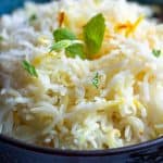 Close up picture of cooked rice in a black bowl with mint garnished on top.