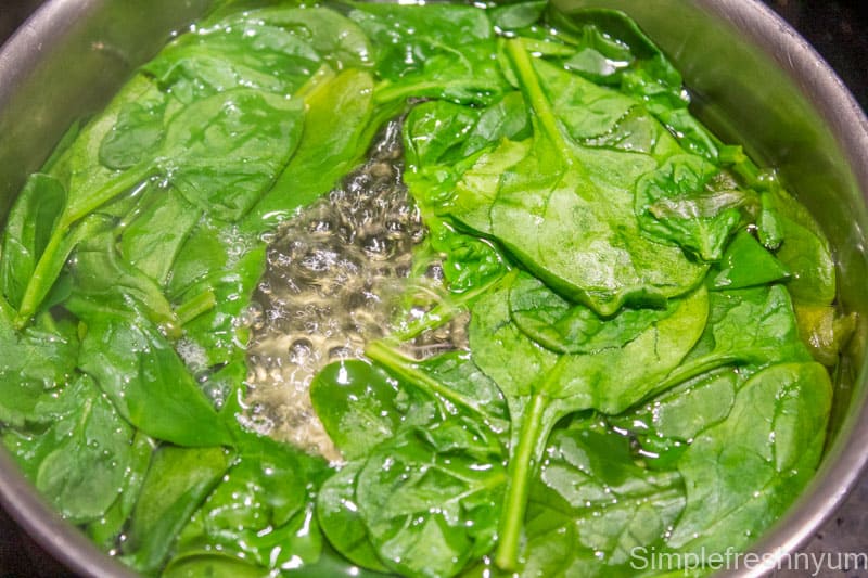 Added fresh spinach to the boiling water to blanch in a stainless steel pot on stove top