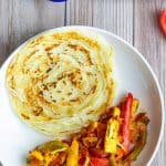 Paneer stir fry served with Paratha on a white plate with a bowl of plain yogurt on the side.