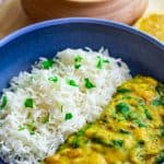 Spinach dal served with white rice on a blue plate with cilantro garnished on top.