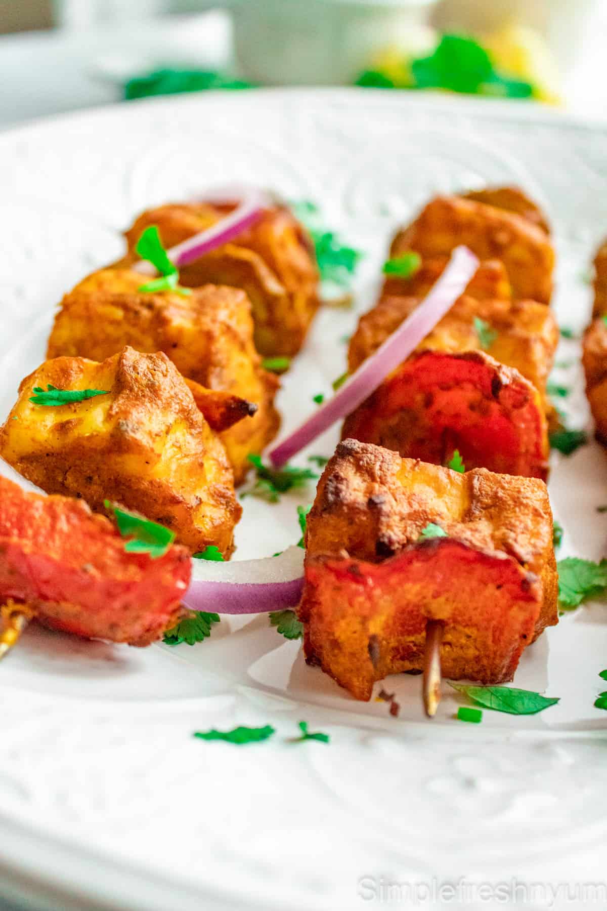 Air fryer grilled paneer tikka served on a white plate with cilantro on top.